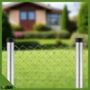 A chain-link fence with two metal posts in the foreground, with a blurred house and garden in the background. Produktbild-Vorschau