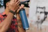 A person is holding a camera and a blue water bottle. Náhled obrázku produktu