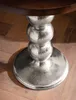 A close-up view of the base of a round table with a wooden top and a metallic pedestal base made of stacked spheres. Voir les images du produit
