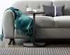 A modern living room scene with a gray sofa, a teal throw blanket, and a small round side table. Produktbild-Vorschau