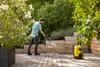 A man is pressure washing a wooden deck in a garden setting. Produktbild-Vorschau