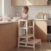 A young child is using a learning tower in a kitchen to help prepare food. Anteprima dell’immagine prodotto