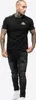 A man wearing a black t-shirt and ripped jeans, standing against a white background. Produktbild-Vorschau
