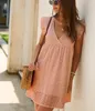 Frau in einem hellen rosa Lochstickerei-Minikleid mit schwingenden Ärmeln, eine geflochtene Strohtasche haltend Produktbild-Vorschau