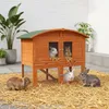 Several rabbits are shown around a wooden multi-level hutch filled with straw.