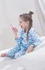 A young girl in pajamas is sitting on a bed, holding a pink walkie-talkie and talking into it. Produktbild-Vorschau