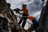 Two climbers are rappelling down a rocky mountain face with a snowy slope in the background. Produktbild-Vorschau