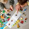 A child and an adult are building LEGO animals and vehicles together on the floor, following instructions. Produktbild-Vorschau