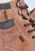 A close-up view of a brown leather boot with black laces and a metal buckle. Produktbild-Vorschau