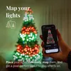 A hand holding a smartphone displaying a Christmas tree light pattern, with a decorated Christmas tree in the background. Náhled obrázku produktu