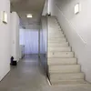 A modern interior hallway with a concrete ceiling and floor, a glass partition, and a concrete staircase. Produktbild-Vorschau