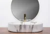 A close-up shot of a marble-patterned vessel sink with a gold faucet, positioned in front of a round mirror against a white wall. Náhľad obrázku produktu