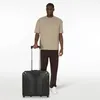 A man stands next to a rolling suitcase. Produktbild-Vorschau