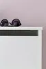 A pair of sunglasses rests on the edge of a white piece of furniture against a light pink wall. Produktbild-Vorschau
