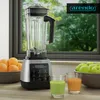 A blender is shown on a kitchen counter with fruit and drinks, with a window in the background. Produktbild-Vorschau