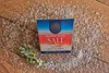 A box of Murray River Salt flakes is placed on a wooden surface scattered with salt, next to a sprig of greenery. Podgląd zdjęcia produktu