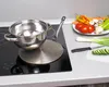 A stainless steel pot sits on an induction cooktop with a metal diffuser plate. Vegetables are prepared on the side. Produktbild-Vorschau