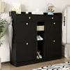 A black shoe cabinet with gold knobs, featuring multiple storage compartments and drawers, is shown in an entryway setting. Produktbild-Vorschau