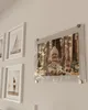 A collection of framed pictures on a wall, with a focus on a framed photo of a baby on a swing. Produktbild-Vorschau