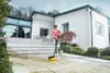 A woman is using a pressure washer on a patio in front of a modern house. Produktbild-Vorschau