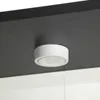 A close-up view of a white LED light fixture mounted on the underside of a black shelf. Podgląd zdjęcia produktu