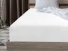 A white fitted sheet on a bed, with a pillow and rumpled sheet in the background. Náhled obrázku produktu