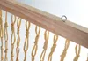 A close-up view of a wooden bar with hanging beige rope strands, possibly part of a hammock or curtain. Produktbild-Vorschau