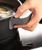 A hand is holding the handle of a black frying pan with a gray silicone grip. The pan contains boiling water. Produktbild-Vorschau