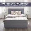 A grey upholstered bed frame with pillows and a blanket in a bedroom setting. Produktbild-Vorschau