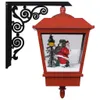 A red Christmas wall lantern with a Santa Claus figurine inside, mounted on a black bracket. Náhľad obrázku produktu