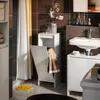 A modern bathroom with dark tiled walls, a white sink and vanity, and a white laundry cabinet with a folded towel. Yellow flip-flops are on the floor. Produktbild-Vorschau