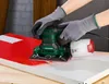 A person wearing gloves is using a green and black orbital sander with a dust collector attached to sand a red and white surface. Produktbild-Vorschau