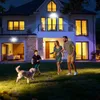 A family and their dog are playing in the yard of a modern house at night, illuminated by outdoor lights. Produktbild-Vorschau
