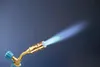 A close-up shot of a blowtorch with a blue flame emitting from the nozzle, against a dark blue background. Voir les images du produit