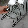 A hand is holding a pot lid over a black metal rack designed to hold pots and lids. Produktbild-Vorschau