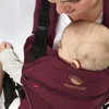 A close-up of a person holding a baby in a baby carrier. Produktbild-Vorschau