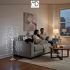 A couple sits on a couch in a living room, looking at a tablet. A decorative LED tree is in the foreground. Podgląd zdjęcia produktu