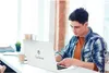 A young man is working on a laptop at a desk in a bright, modern office or home setting. Produktbild-Vorschau