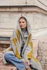 A woman wearing a hooded cardigan and jeans sits on stone steps outdoors. Produktbild-Vorschau