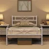 A white metal bed frame with a decorative headboard and footboard, set up in a bedroom with nightstands and lamps. Podgląd zdjęcia produktu