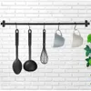 A black metal kitchen utensil rack with various utensils and mugs hanging from it, mounted on a white brick wall. Náhled obrázku produktu