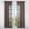 A window with brown curtains and sheer voile panels, showing a view of trees and water outside. Produktbild-Vorschau