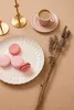 A still life arrangement of macarons, coffee, and dried lavender on a beige surface. Produktbild-Vorschau