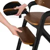 Close-up of hands adjusting a wooden footrest on a black high chair. Voir les images du produit