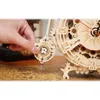 A hand is shown adjusting the pendulum of a wooden mechanical clock. Produktbild-Vorschau