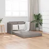 A grey sofa bed is unfolded in a room with light wood flooring, a white window with blinds, and a tall green plant in a pot. Produktbild-Vorschau