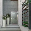 A modern entryway with two tall white planters flanking a sleek gray door, set against a textured gray wall and concrete steps. Produktbild-Vorschau
