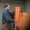 A man in overalls is working with an orange industrial machine. Voir les images du produit