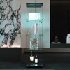 A modern glass display shelf with illuminated shelves, featuring books, a piece of art, and two bottles. Náhled obrázku produktu