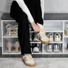 A person is sitting on a shoe cabinet and tying their shoe. Produktbild-Vorschau